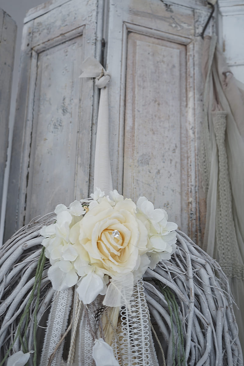 Kranz aus Zweigen mit einer cremefarbenen Rose und dekorativen Bändern im Hintergrund einer shabby-chic Wand
