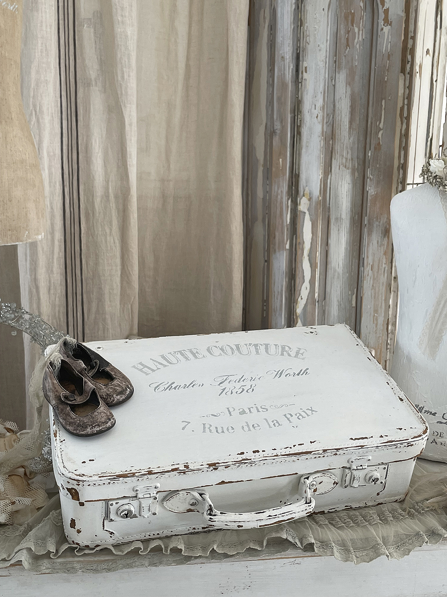 Weißer Vintage-Koffer mit dem Aufdruck Haute Couture und alten Kinderschuhen darauf.