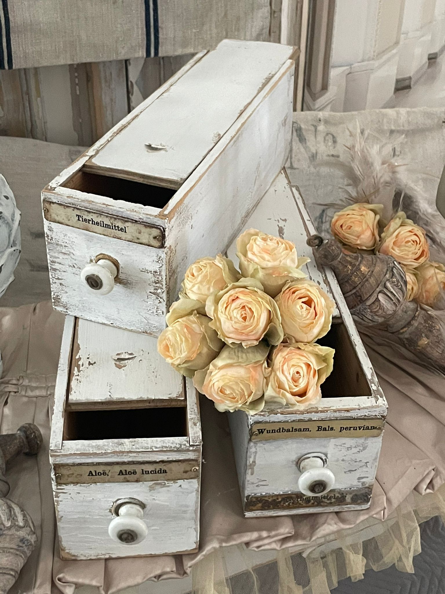 Drei alte Holzkisten mit beschrifteten Schubladen und einer Blume aus Rosen