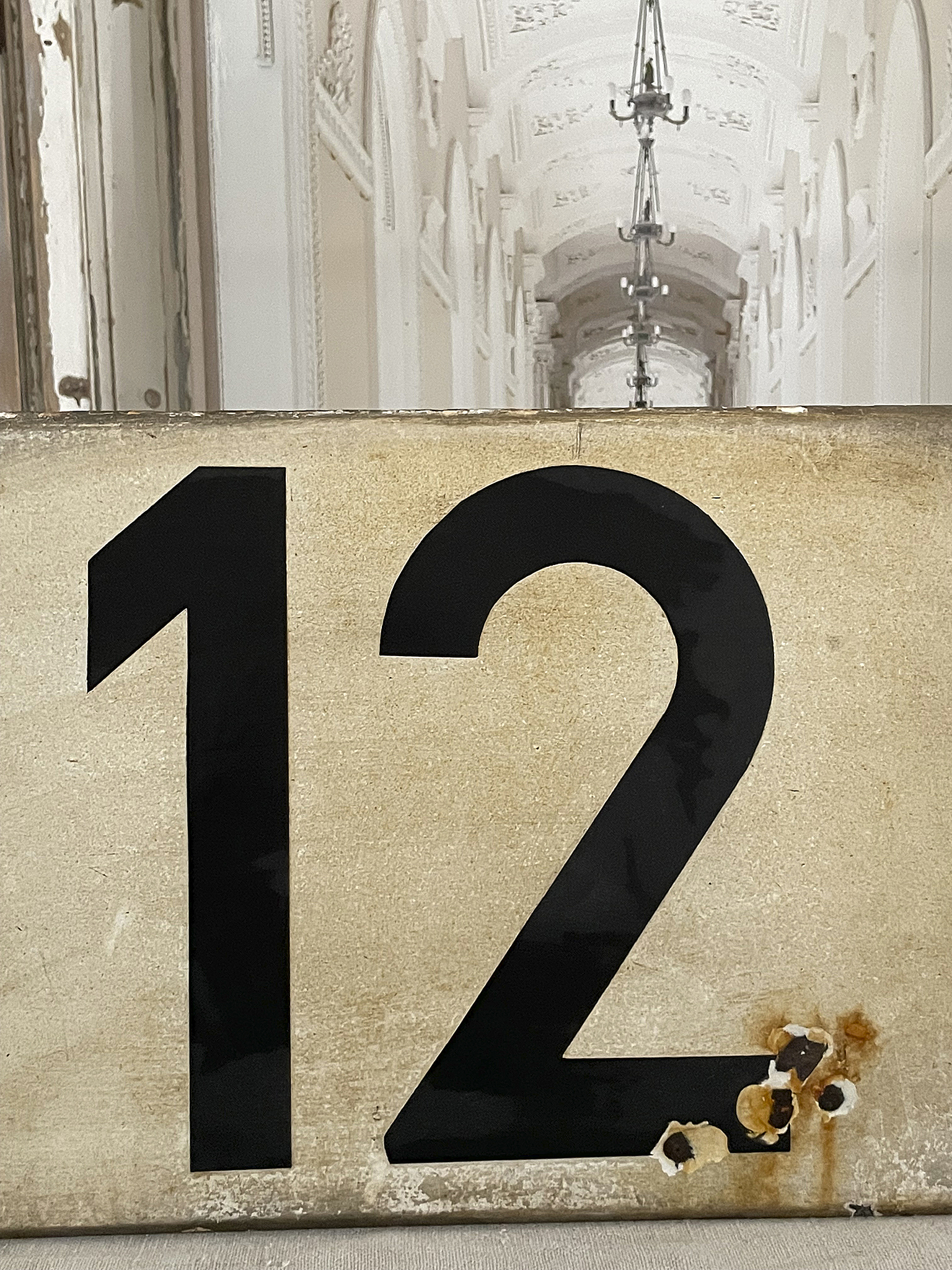 Die Hausnummer 12 auf einem vergilbten Schild in einem eleganten Flur