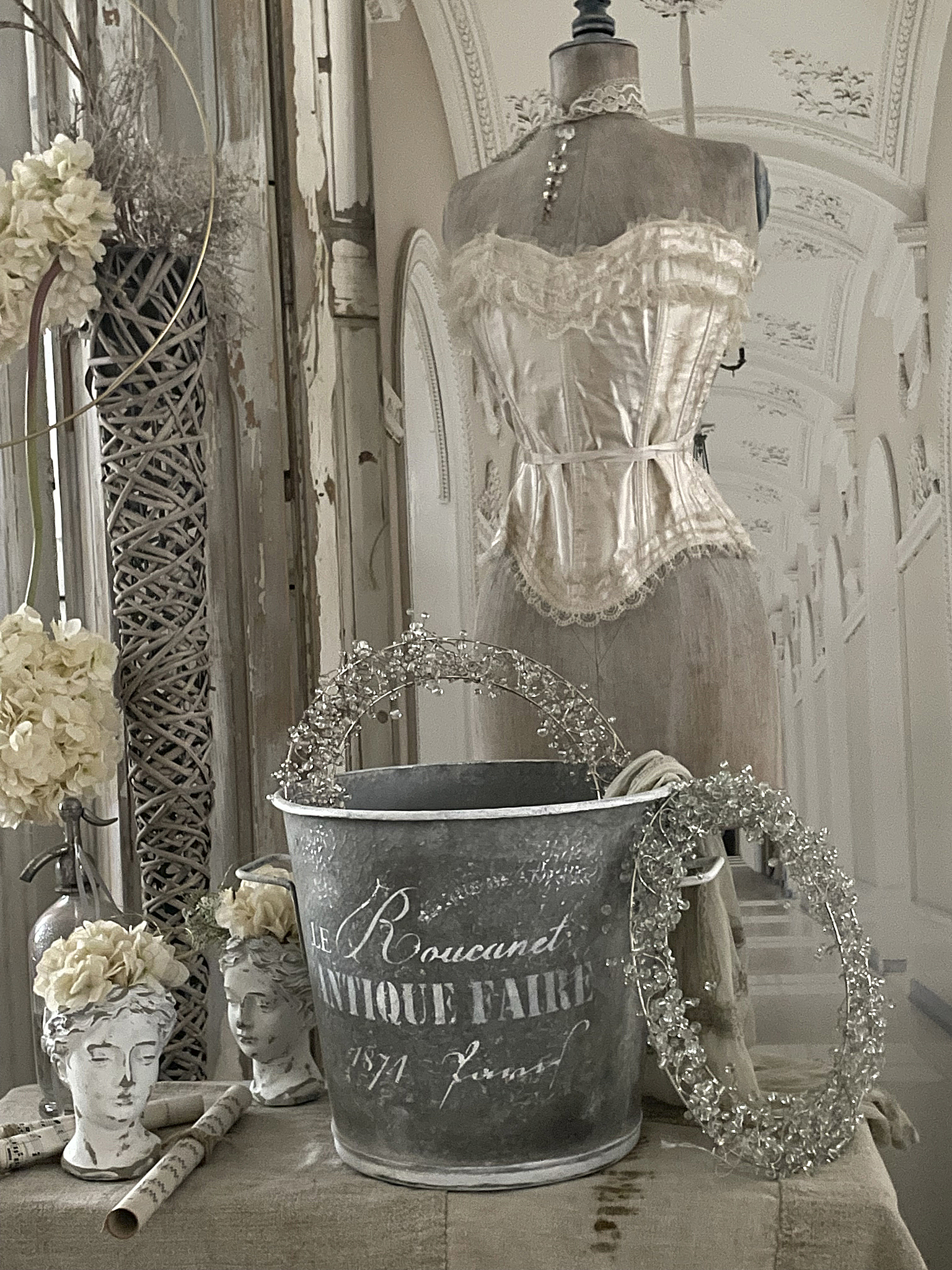 Elegante Vintage-Dekoration mit Spitzenkorsetts und antiken Accessoires Detailansicht einer Vintage-Dekoration mit einem Spitzencorsett, antikem Eimer und Blumenschmuck auf skulpturalen Köpfen.