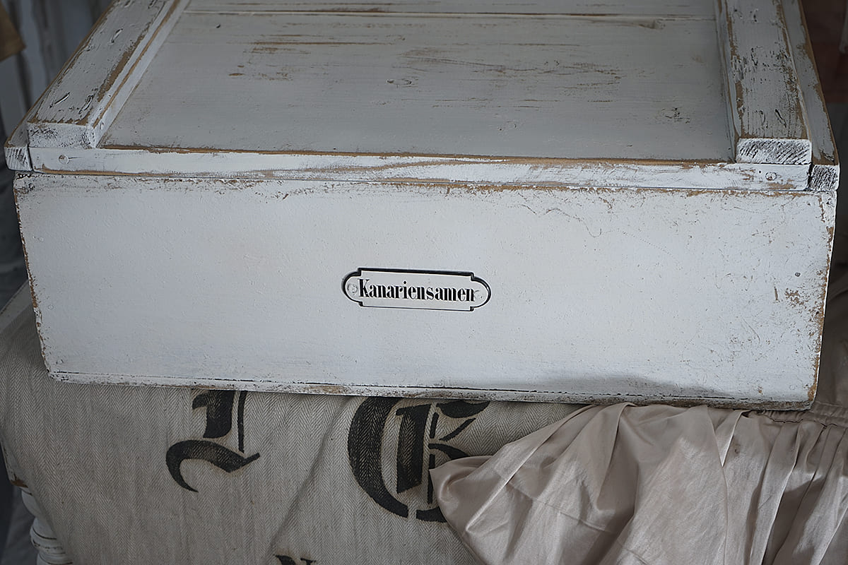 Dekorative Holzkiste in distressed White-Optik mit der Beschriftung Kanariensamen