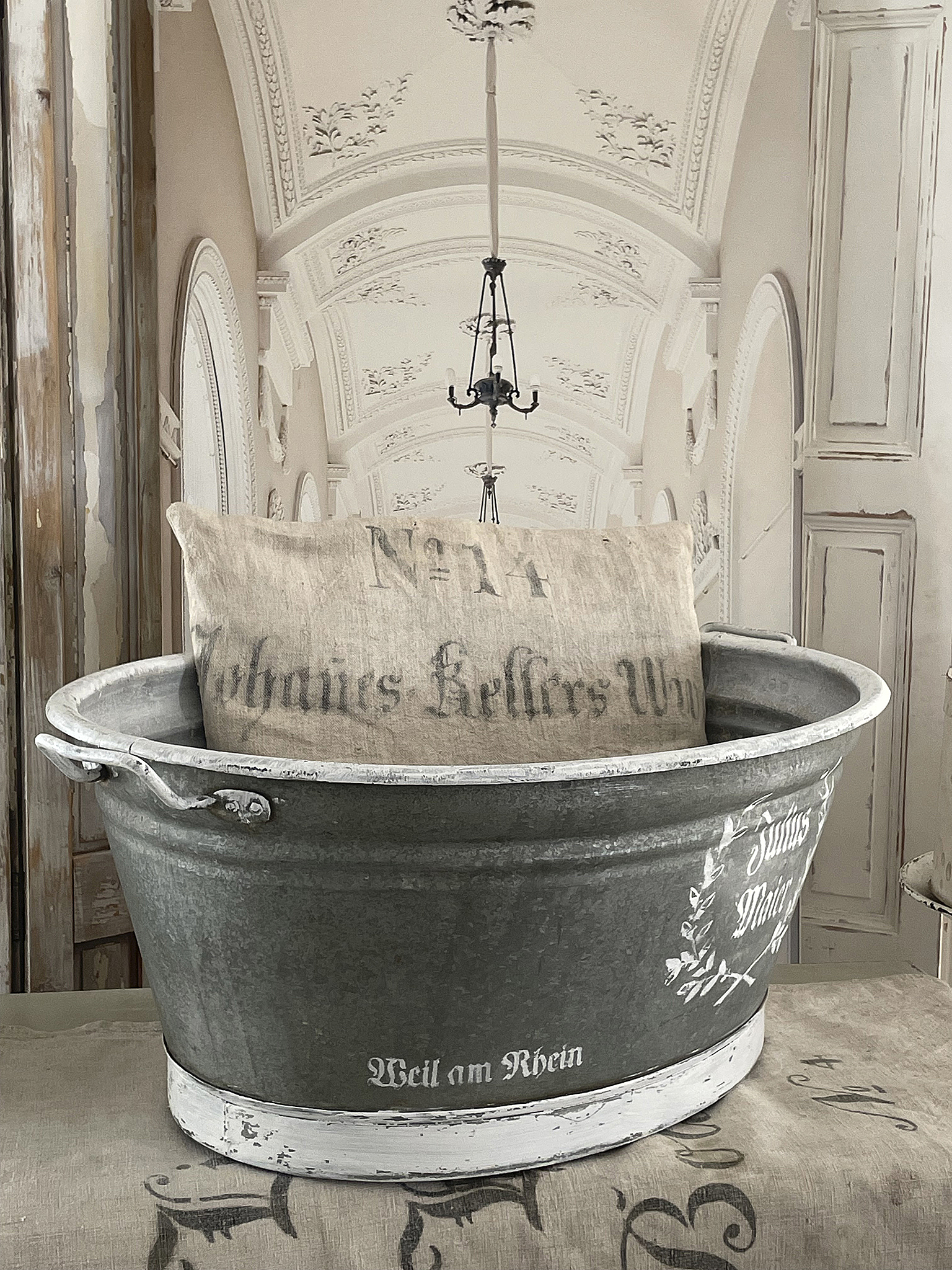 Dekorativer Zinkbehälter mit Kissen im Vintage-Stil Zinkwanne mit Kissen im Landhausstil auf einem Tisch vor einem eleganten Hintergrund