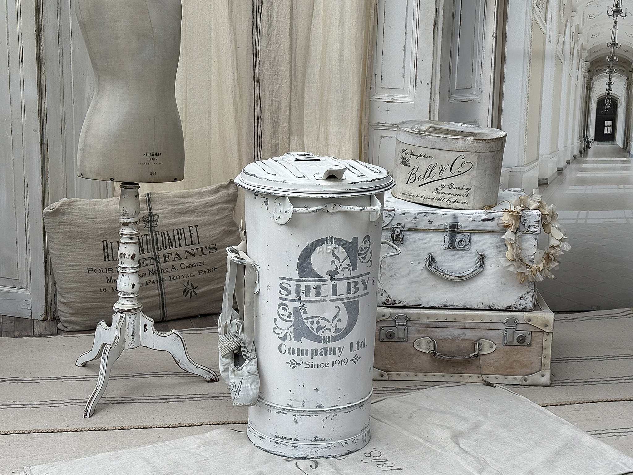 Stilvolle Dekoartikel für ein vintage Zuhause Dekorative Objekte wie eine weiße Mülltonne, ein Schneiderpuppenständer und verschiedene alte Koffer in einem eleganten, hellen Raum.