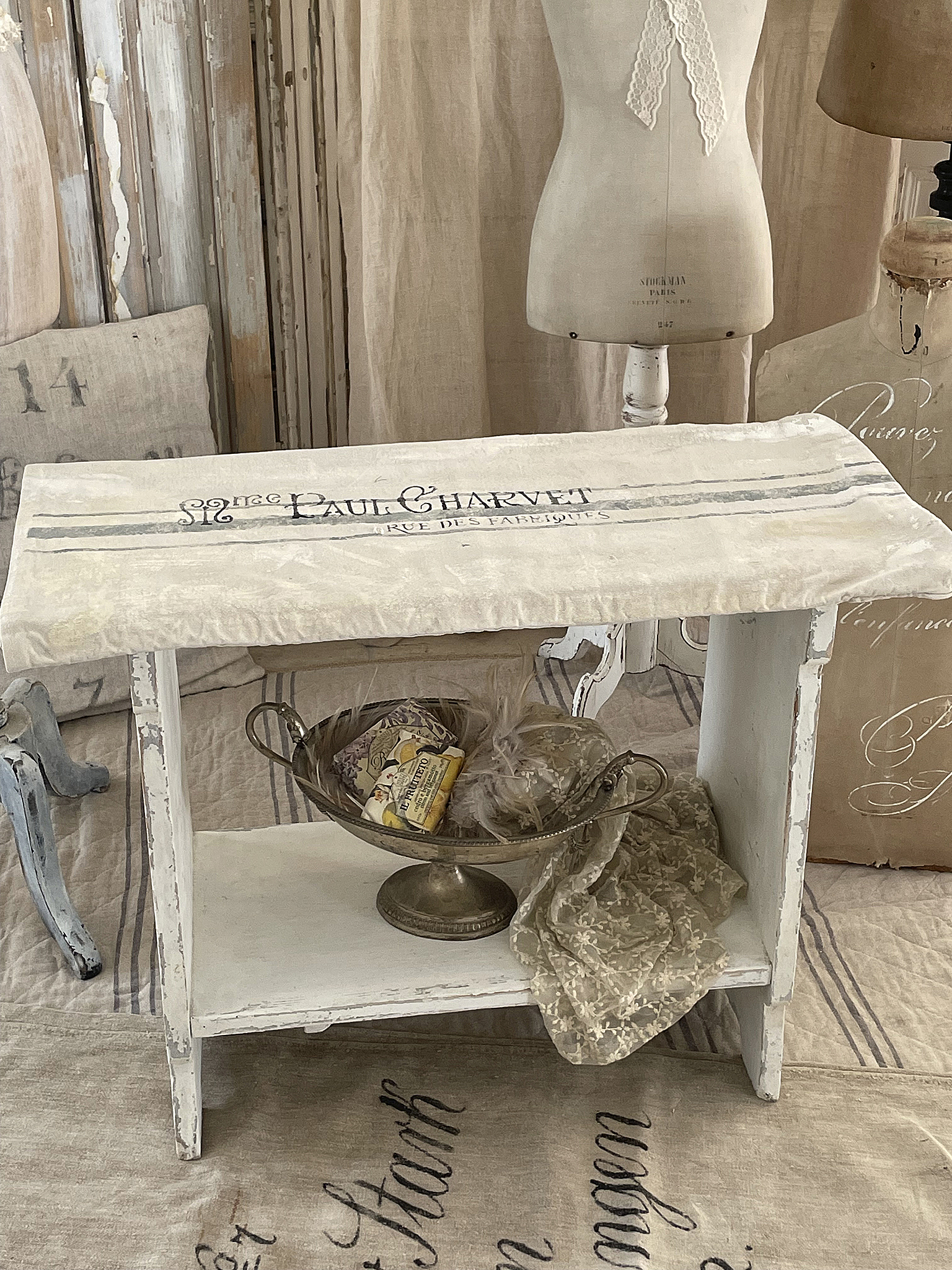 Antiker Beistelltisch im Shabby-Chic-Stil mit Dekoration Ein antiker Beistelltisch im Shabby-Chic-Stil, dekoriert mit einer silbernen Schüssel und Stoffen.