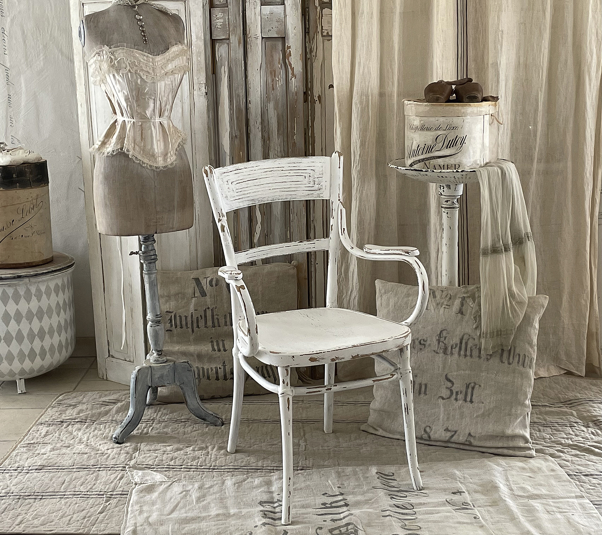 Klassischer weißer Stuhl im Vintage-Stil mit Mannequin und Accessoires Ein stilvolles Interieur mit einem weißen Vintage-Stuhl, einem Mannequin und dekorativen Gegenständen.