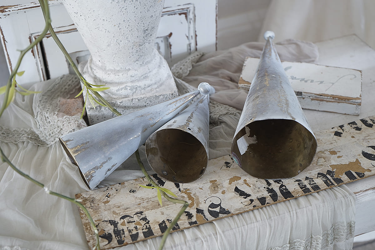 Zwei stilvolle Metallgefäße im Vintage-Stil neben einer weißen Vase und einer dekorativen Stoffunterlage