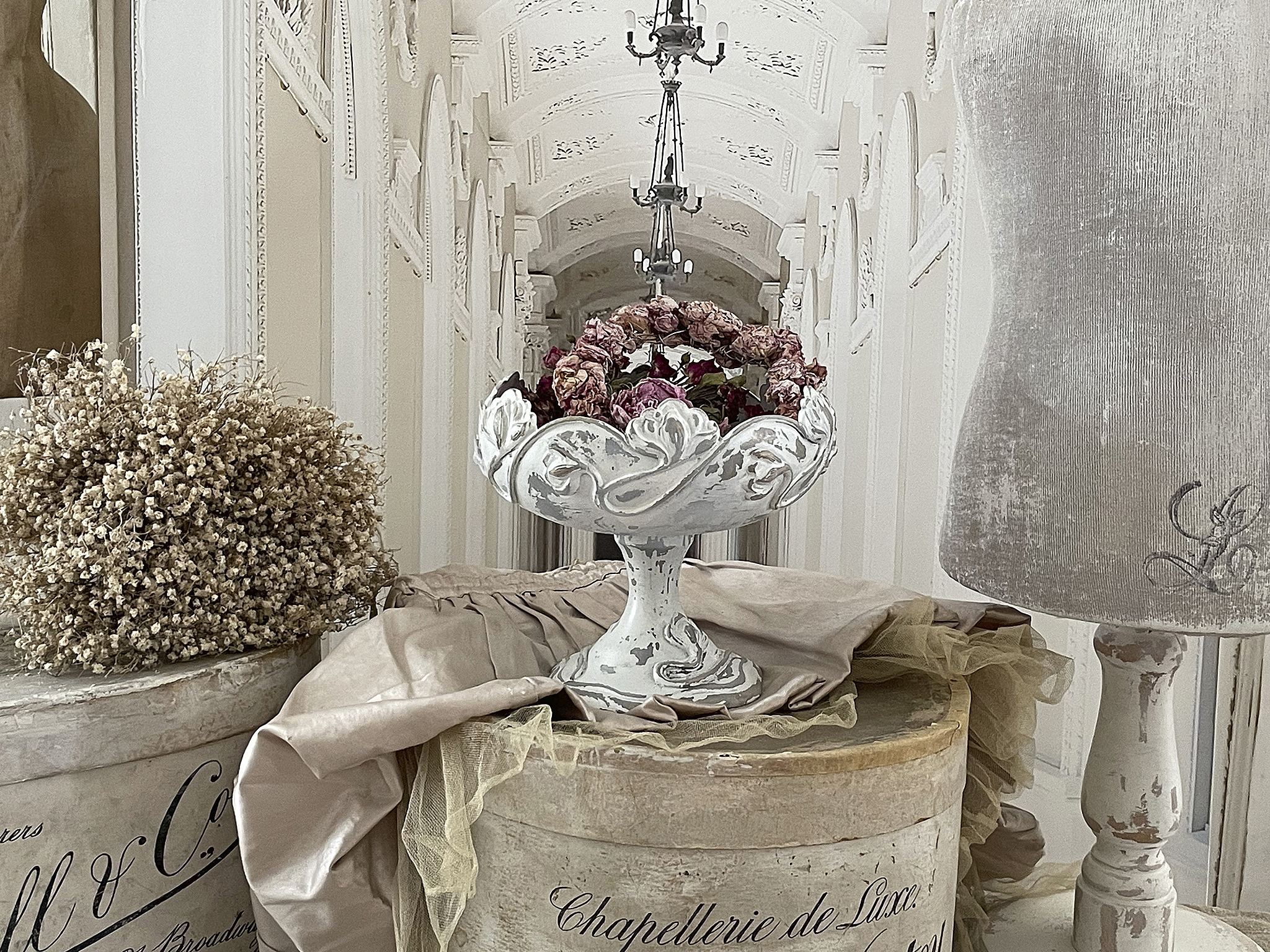 Dekorative Blumenschale aus Weiß mit getrockneten Rosen, umgeben von stilvollen Accessoires in einem eleganten Raum