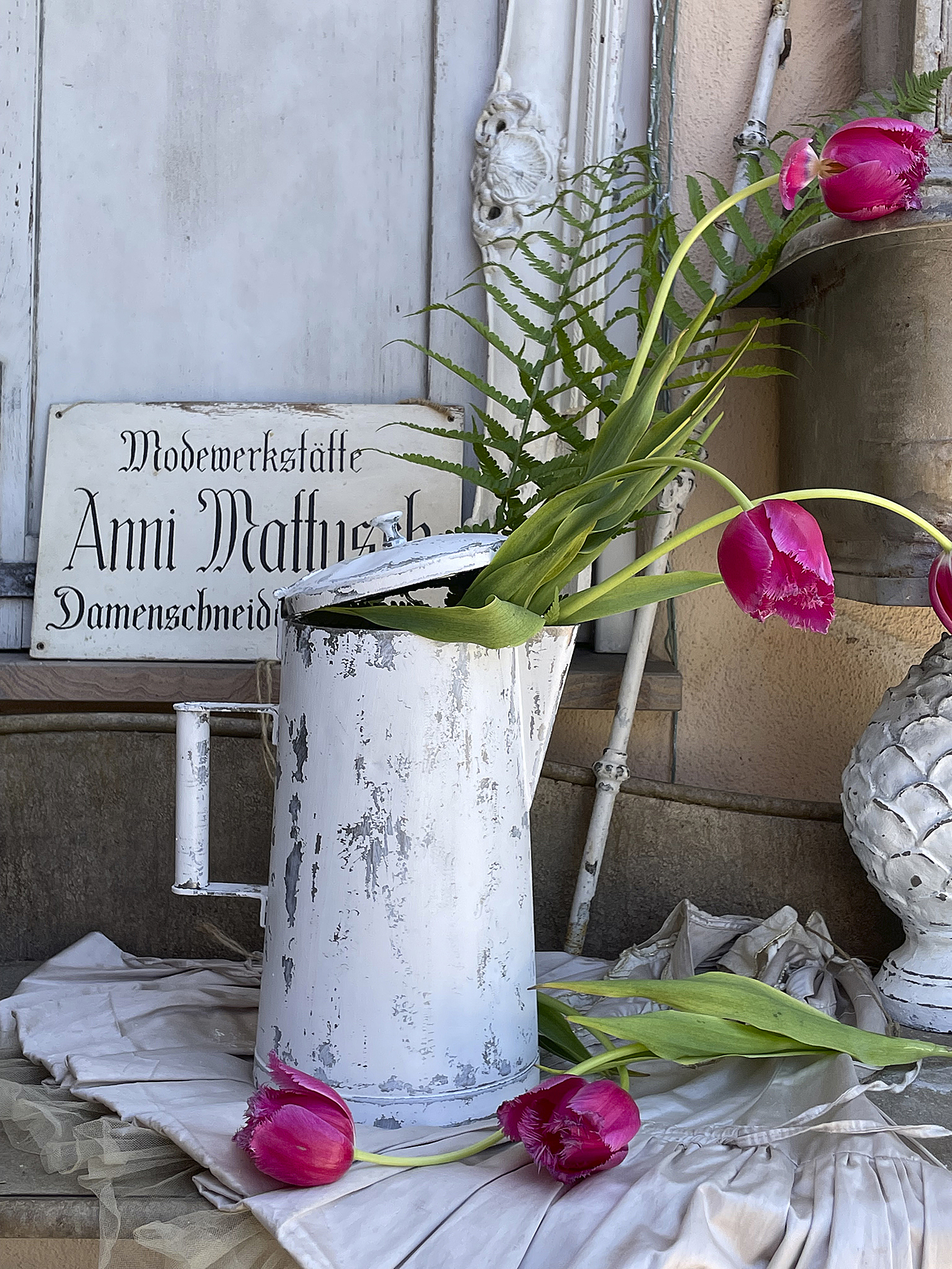 Blumenvase aus Metall mit Tulpen und Farn in romantischem Ambiente Metallkanne als Blumenvase mit pinken Tulpen und Farn, als dekorativer Blickfang