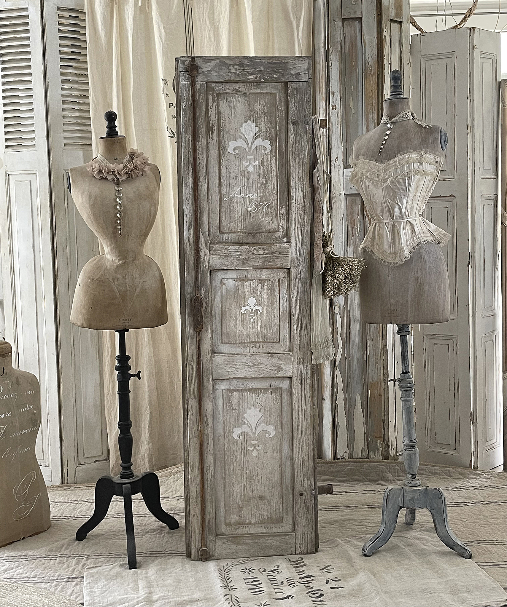 Vintage Schneiderpuppen und weiße Holztür im Atelier Zwei elegante Schneiderpuppen in einem stilvollen Atelier mit einer antiken Holztür im Hintergrund.