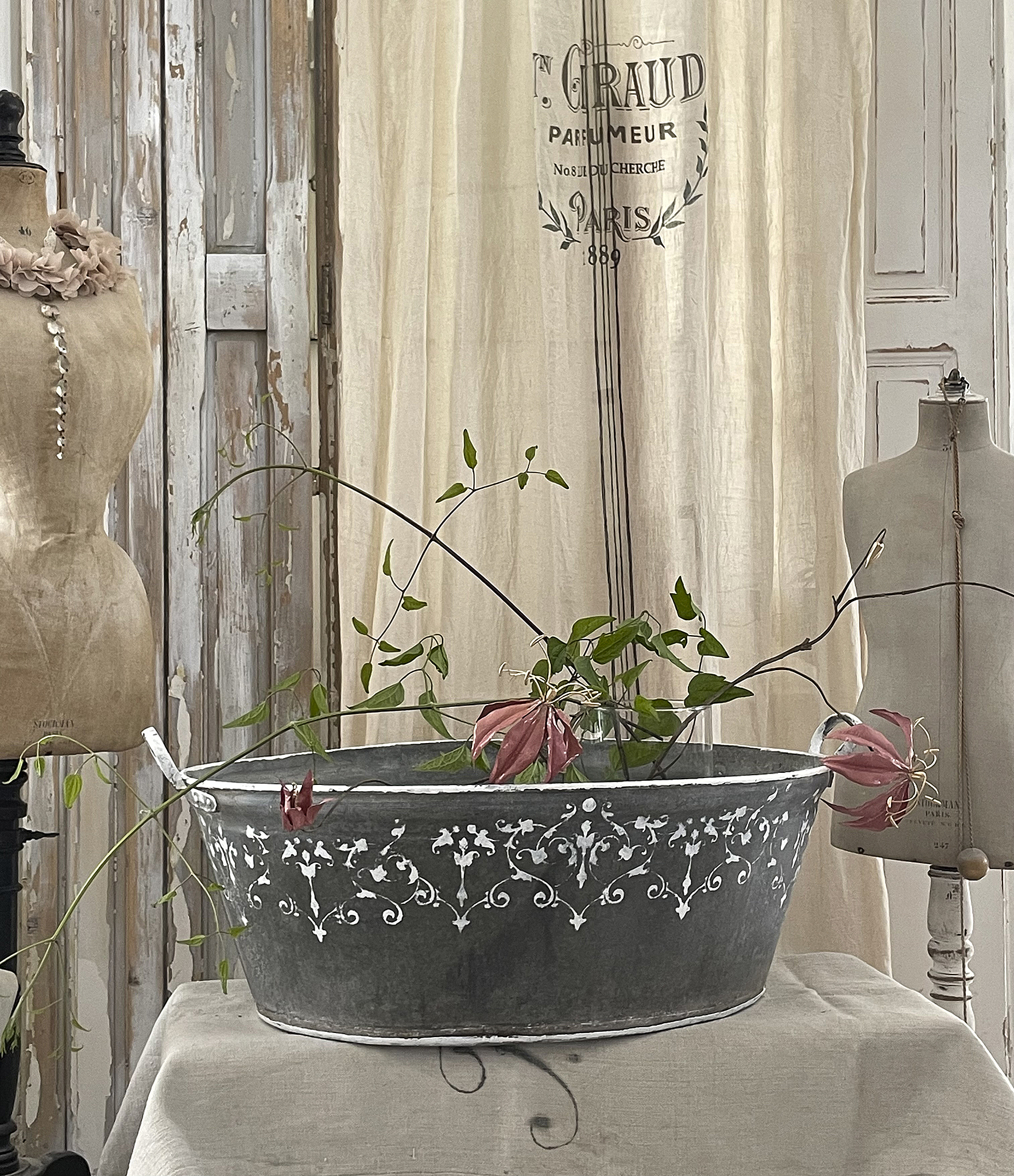 Dekorativer Altmetall-Eimer mit floralen Elementen und Mannequins Eleganter Altmetall-Eimer mit Pflanzen und dekorativer Gestaltung in einem stilvollen Raum