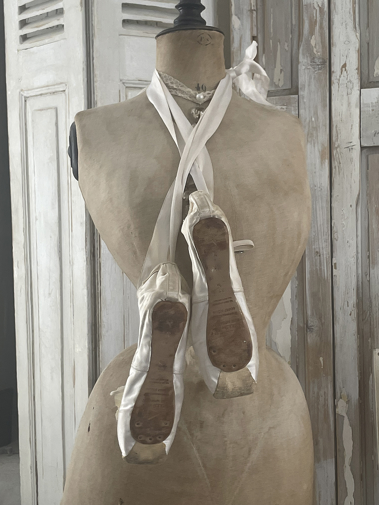 Vintage Ballettschuhe an einer Schneiderpuppe Ballettschuhe hängen an einer Schneiderpuppe, umgeben von einem rustikalen Hintergrund.
