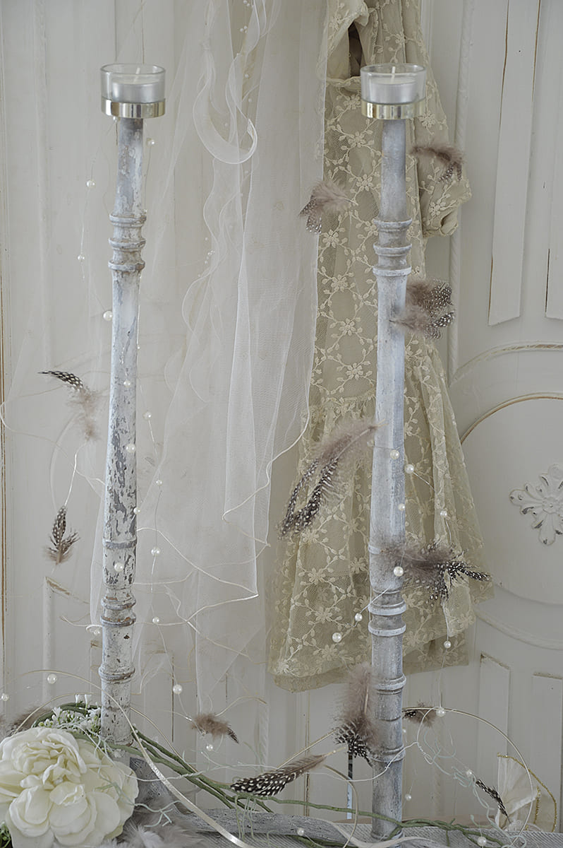 Zwei dekorative Kerzenständer mit Feder- und Perlenschmuck vor einem eleganten Kleid.
