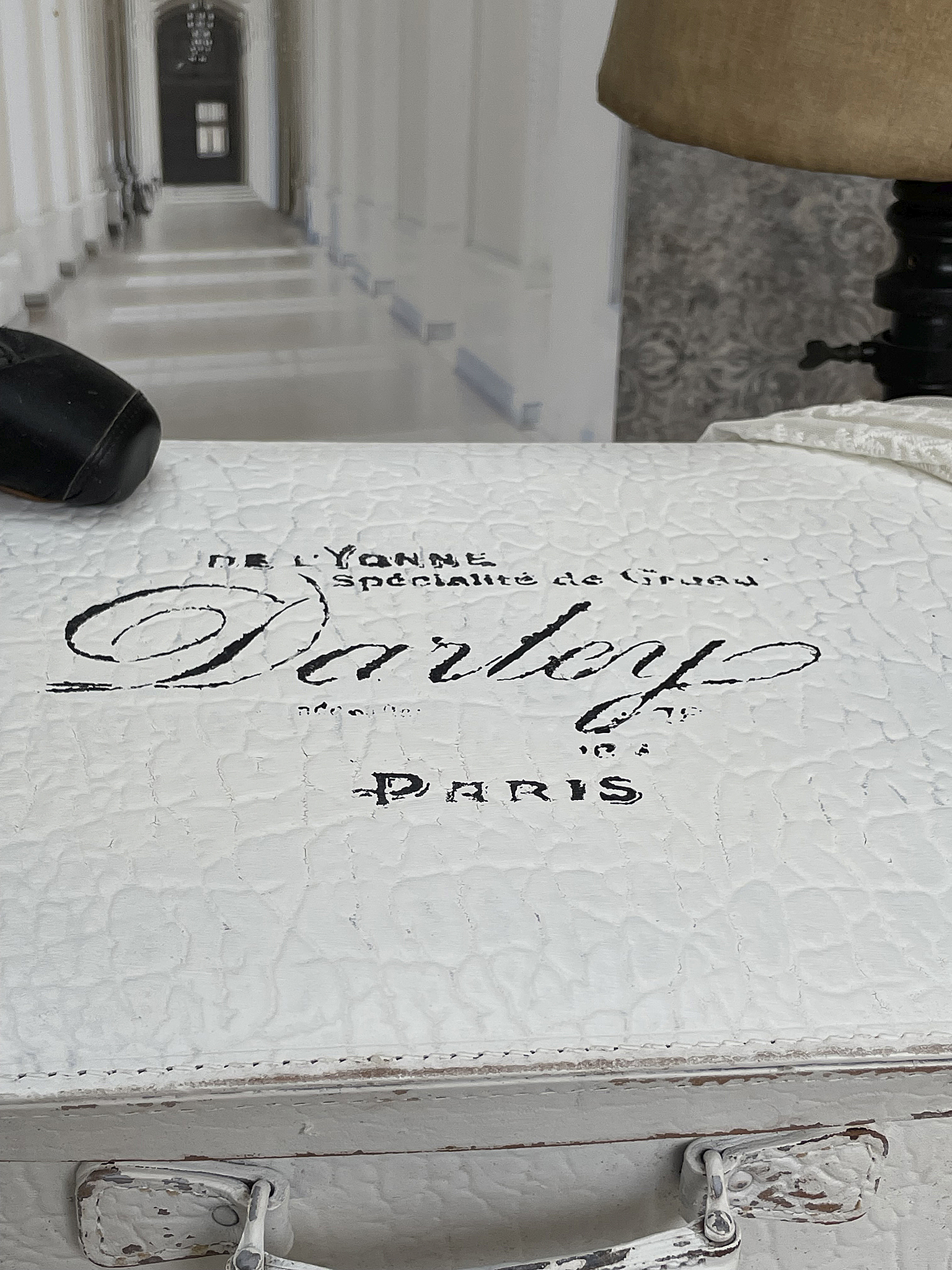 Vintage Aufbewahrungskoffer mit französischer Beschriftung Detailansicht eines weißen Vintage-Koffers mit der Aufschrift "Darley" und einer eleganten Textur.