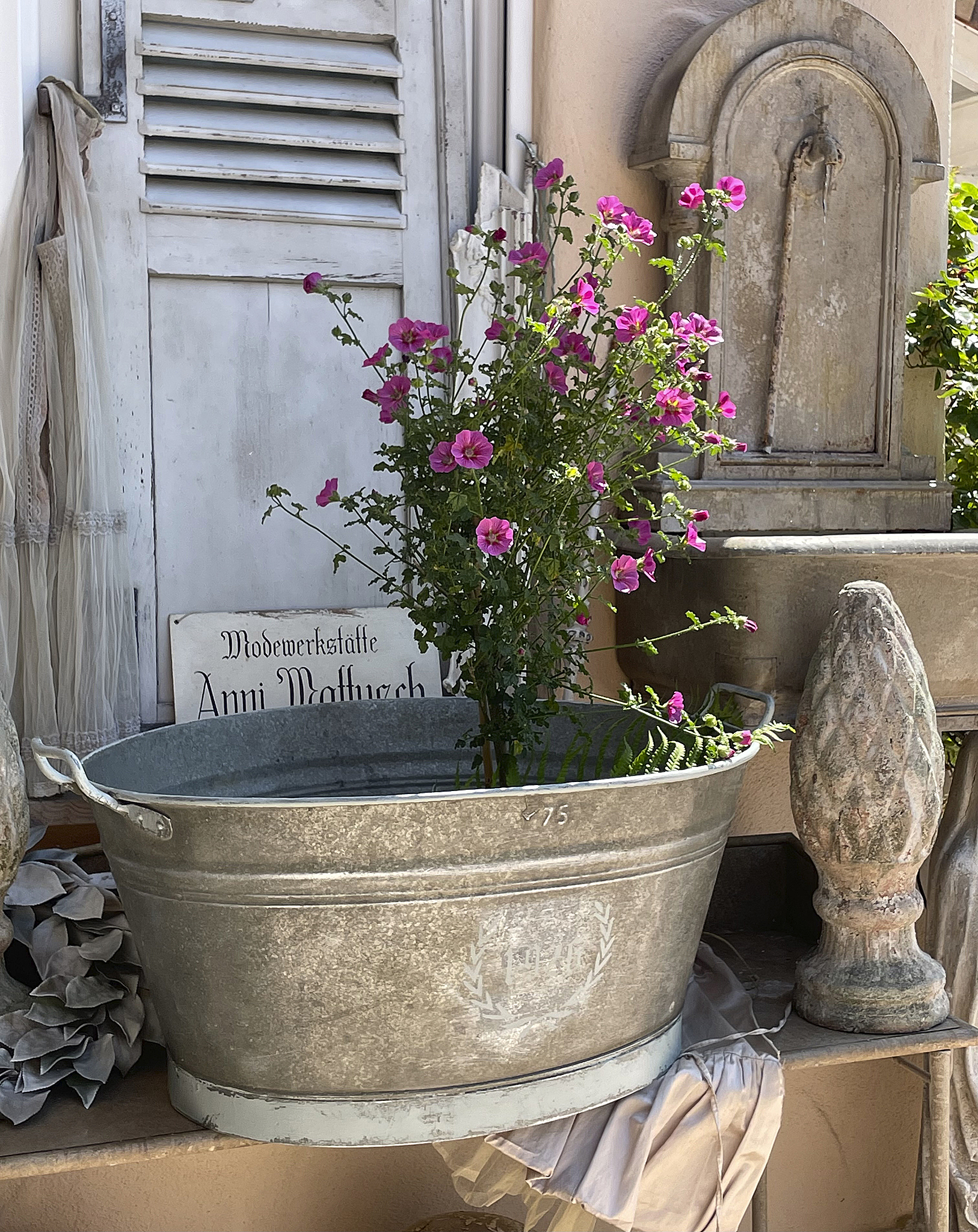 Blumentopf aus Metall mit bunten Blumen vor einer alten Wand Metallbehälter mit pinken Blumen, dekorativ platziert vor einer historischen Tür.