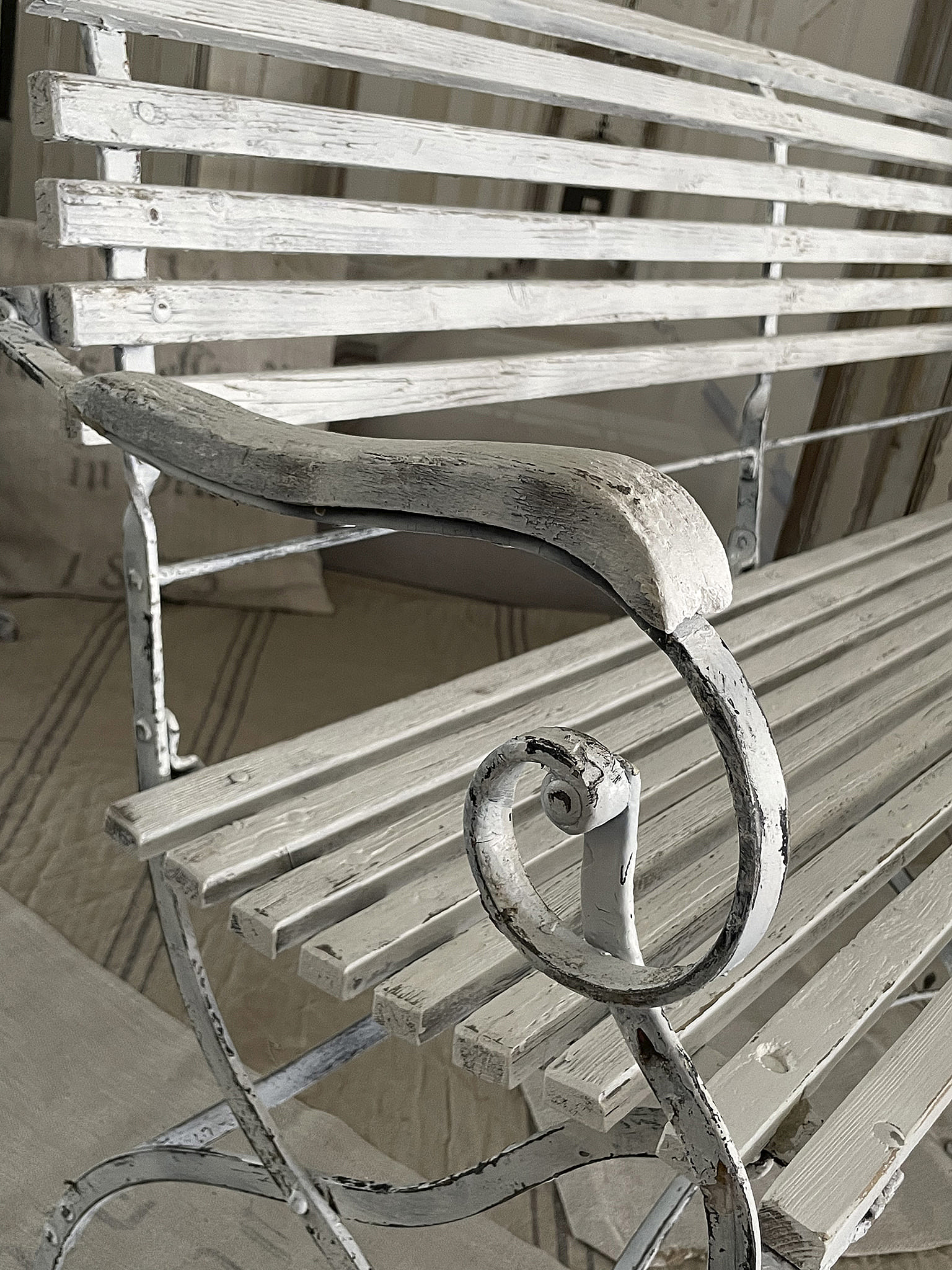 Detailansicht einer weißen Gartenbank aus Metall und Holz mit geschwungener Armlehne