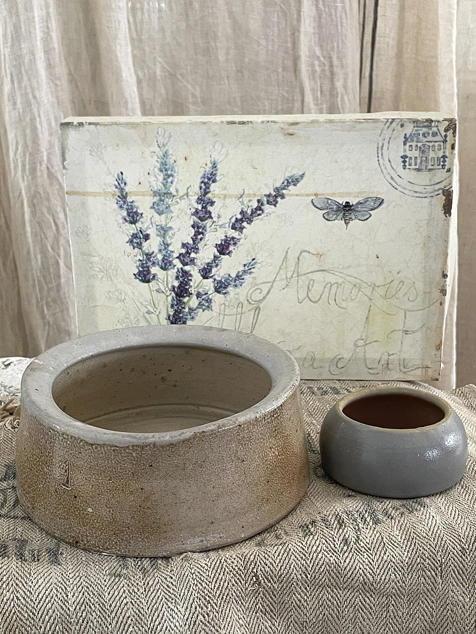 Zwei Keramiktöpfe in neutralen Farben, einer groß und der andere klein, auf einem Tisch mit einem kunstvollen, vintage Hintergrund.