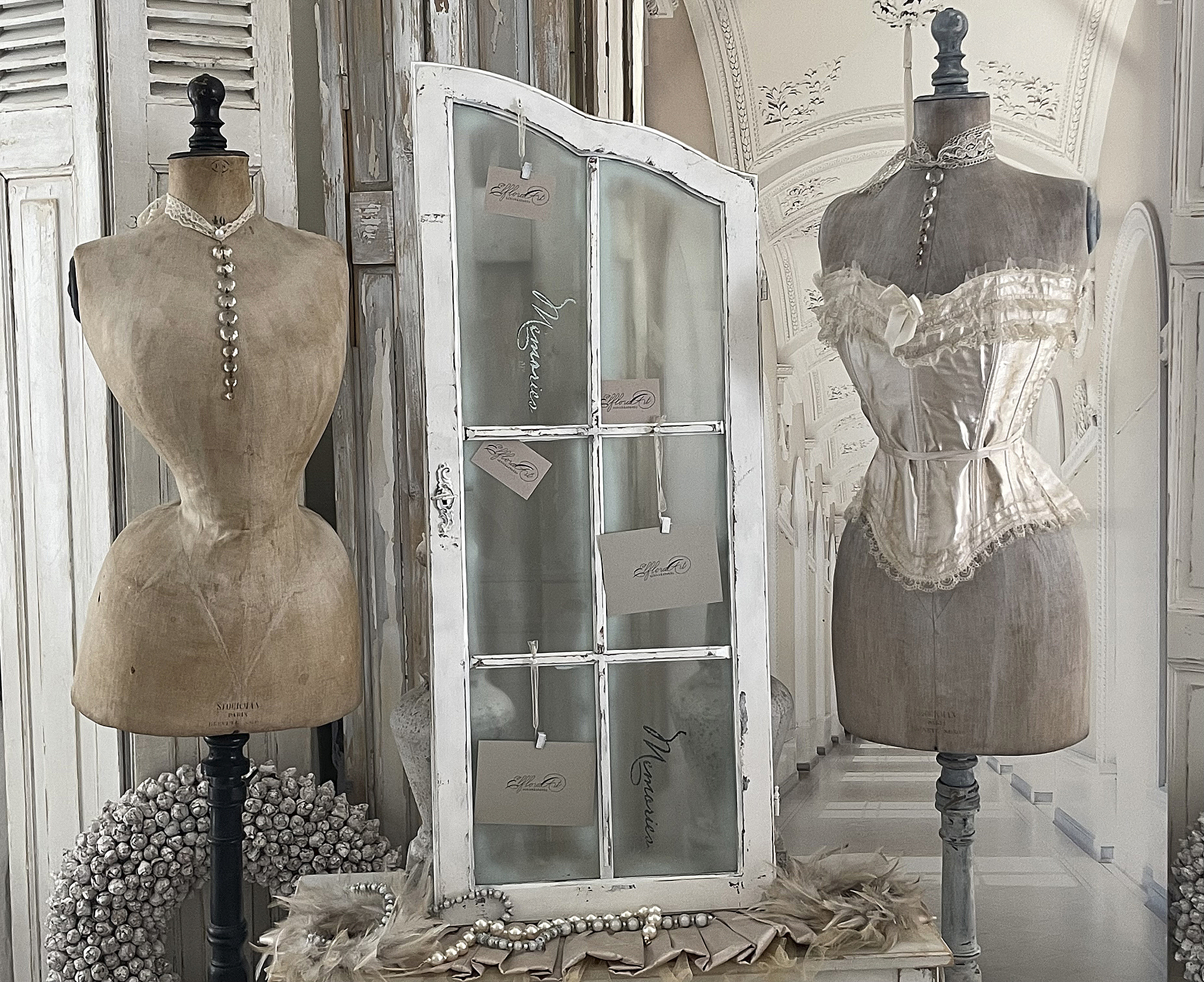 Elegante Schneiderpüppchen mit vintage Korsett und Schmuck Zwei Schneiderpuppen mit einem weißen Korsett und einer Schmuckkette, sowie einem dekorativen Fenster im Hintergrund.