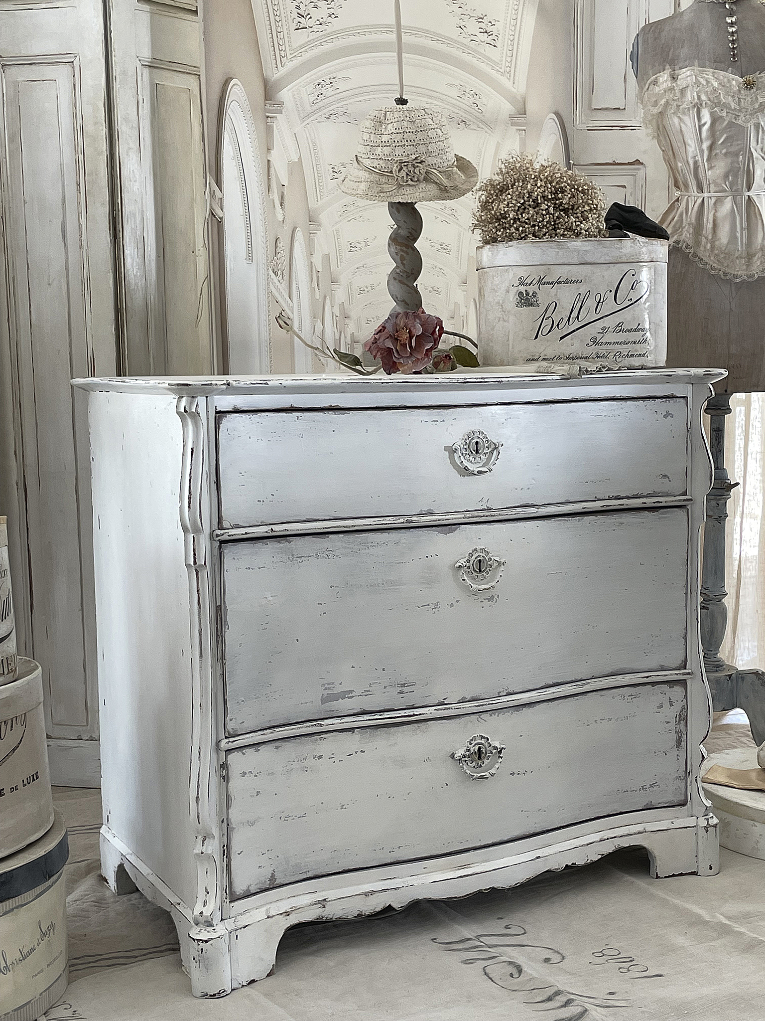 Wunderschöne antike Kommode im Shabby Chic Stil, dekoriert mit floralen Elementen und einer eleganten Umgebung.
