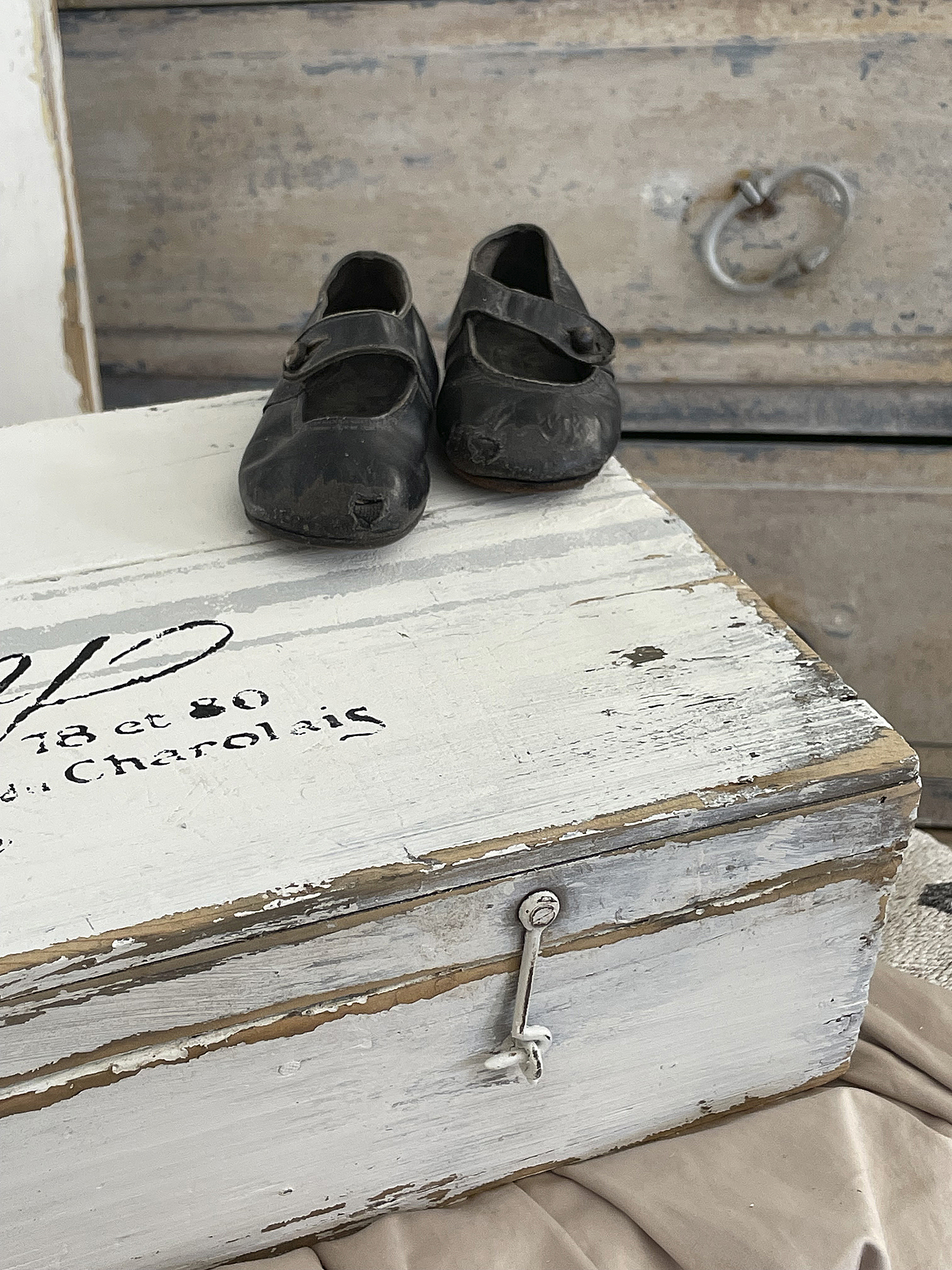 Schwarze Kinderschuhe auf einer rustikalen Kiste Detailaufnahme von schwarzen Kinderschuhen auf einer weißen, beschädigten Kiste