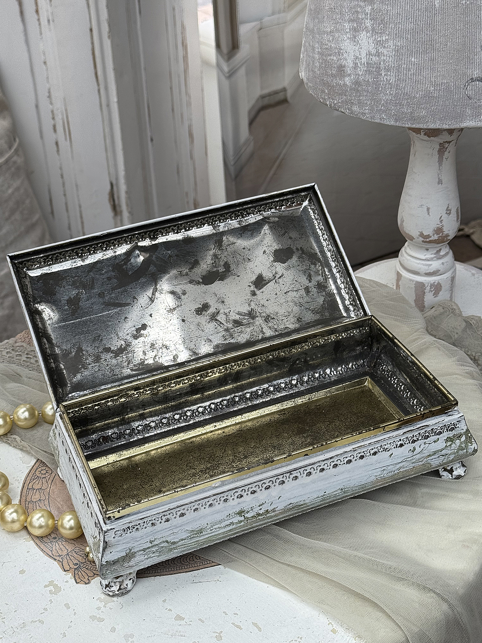 Elegante Speicherbox aus Metall mit aufklappbarem Deckel Vintage metallene Schmuckbox mit goldener Innenseite, auf einem Tisch mit einer Perlenkette.