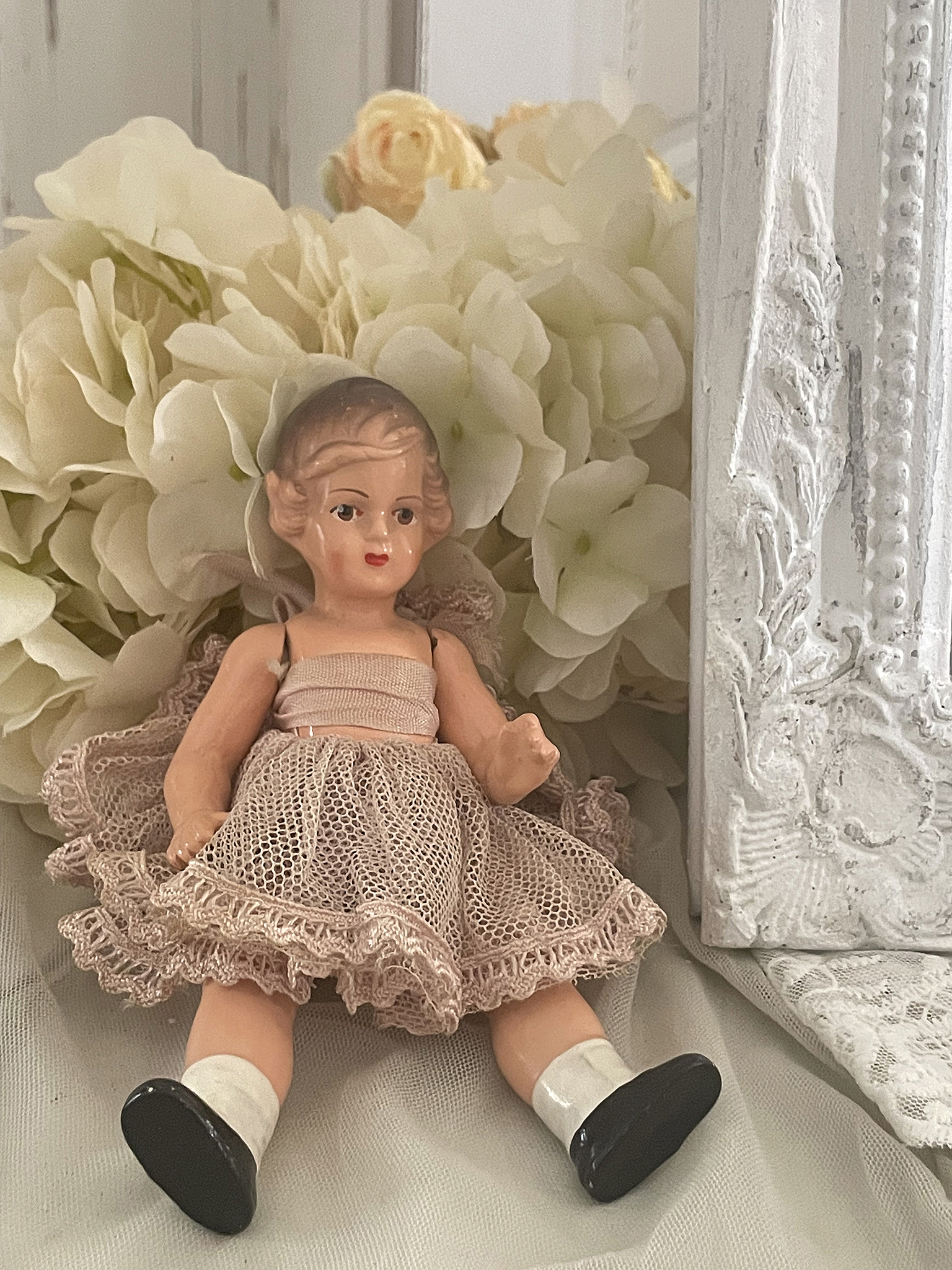 Vintage Puppe im hübschen Kleid vor Blumenarrangement Antike Puppe mit hellem Kleid, umgeben von weißen Blumen