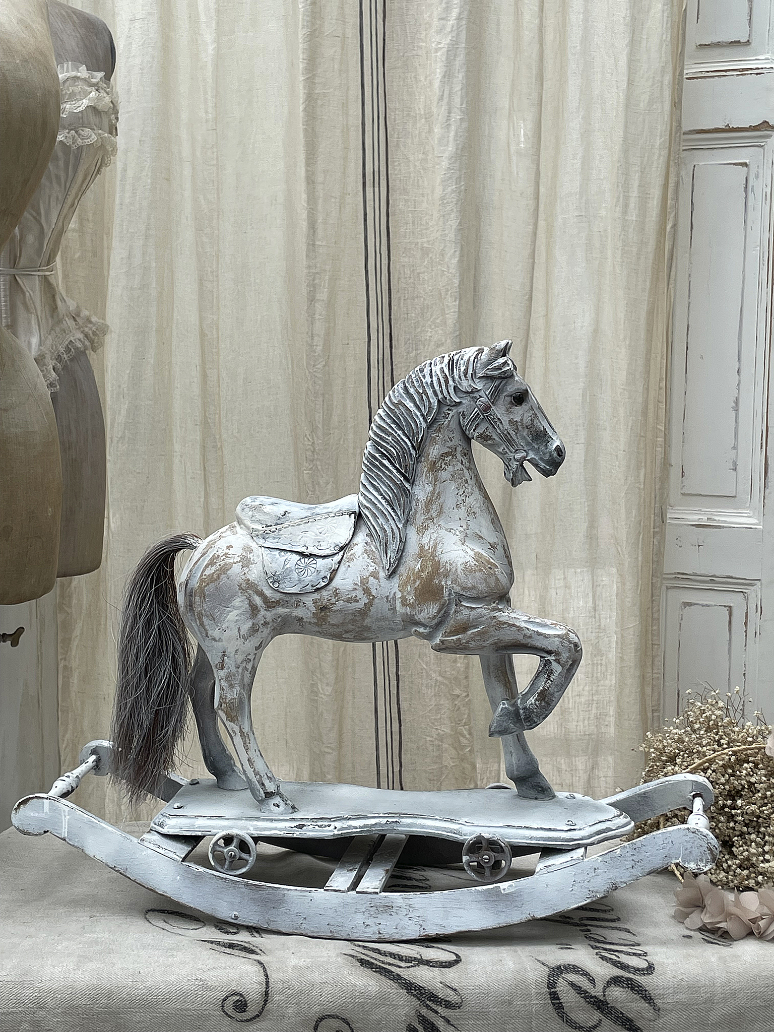 Ein nostalgisches Schaukelpferd aus Holz mit weißer Patina auf einem eleganten Hintergrund.