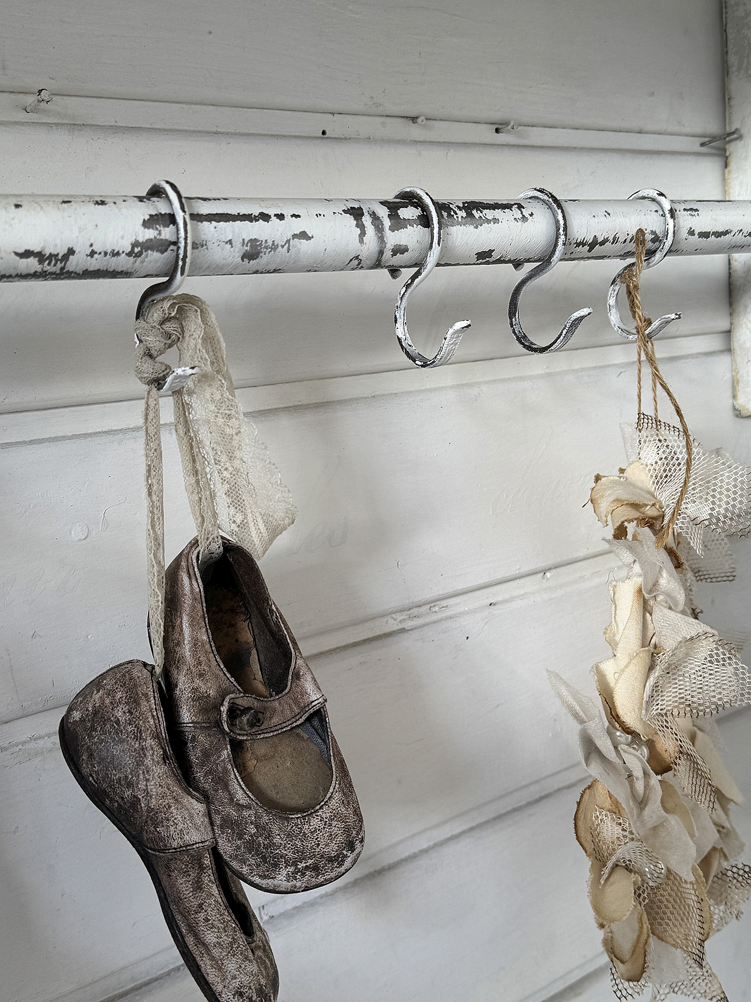 Antike Kinderschuhe und Dekoration an einem Haken Hängende alte Kinderschuhe und Dekoration an einem weißen Metallhaken