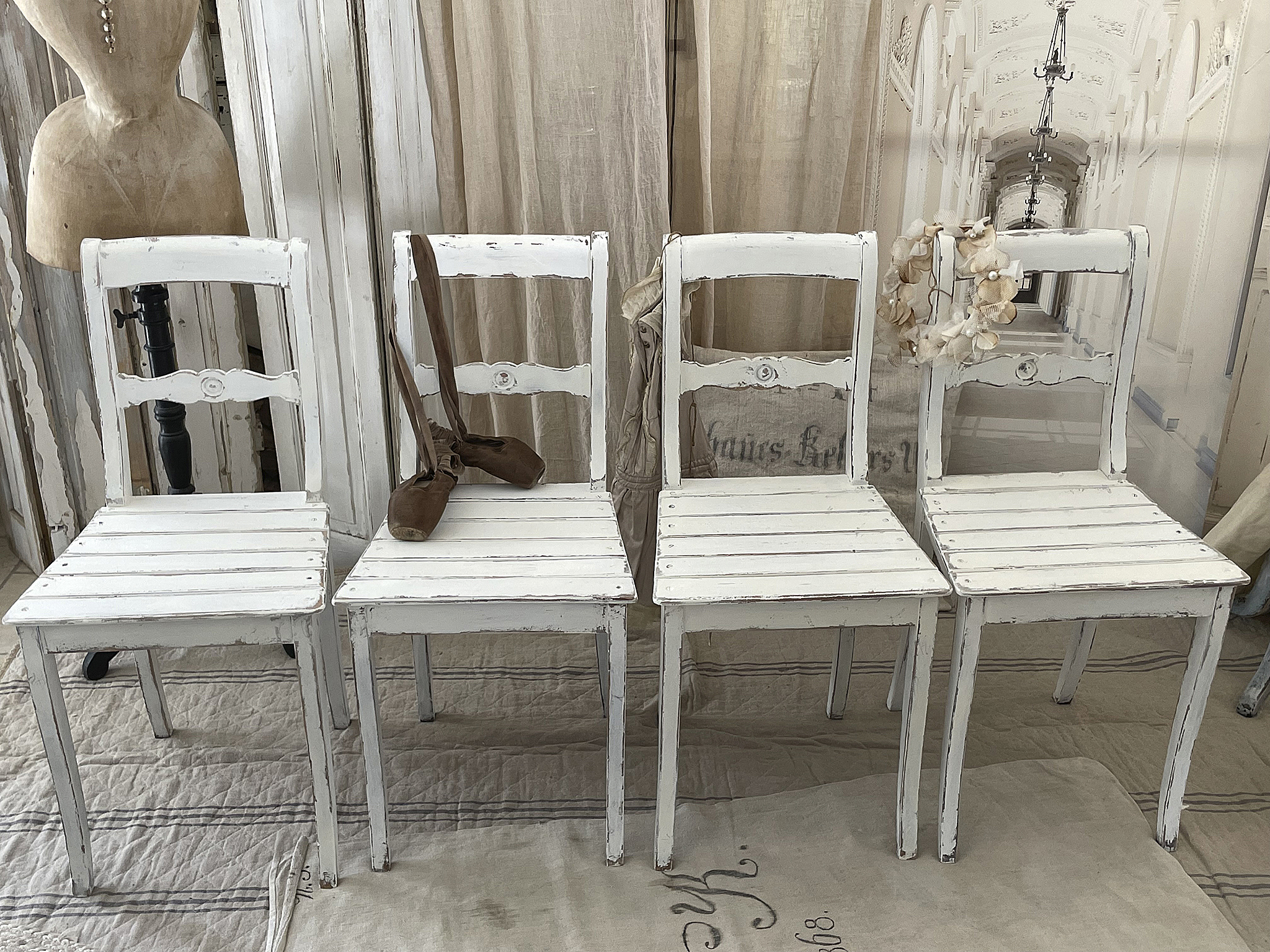 Vintage weiße Stühle als stilvolle Raumdekoration Vier Vintage weiße Stühle mit Ballettschuhen und dekorativem Kranz, perfekt für eine ansprechende Inneneinrichtung