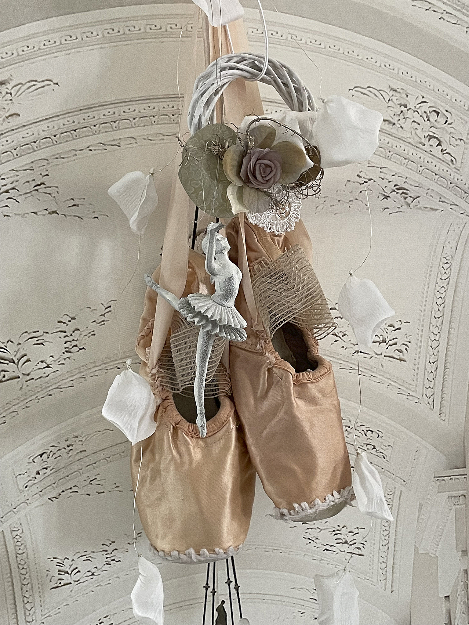 Dekorative Ballettschuhe mit einem weißen Balletttänzer und floralem Kranz Schöne Ballettschuhe hängen dekorativ mit einem Tänzer und Blumen im Hintergrund
