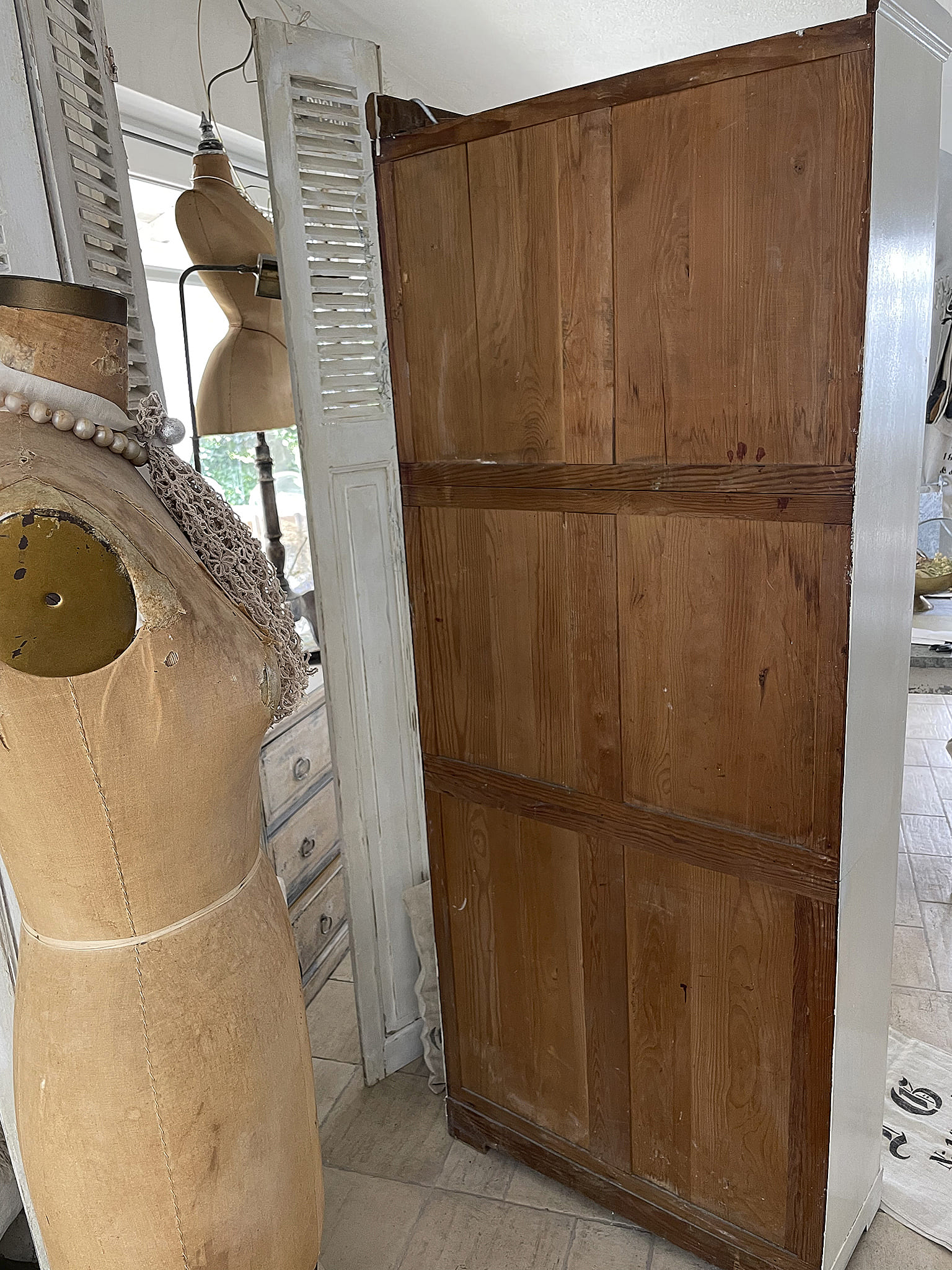 Antiker Schrank in einem stilvollen Raum mit Schneiderpuppe Antiker Holzschrank neben einer Schneiderpuppe und Fenster mit Jalousien