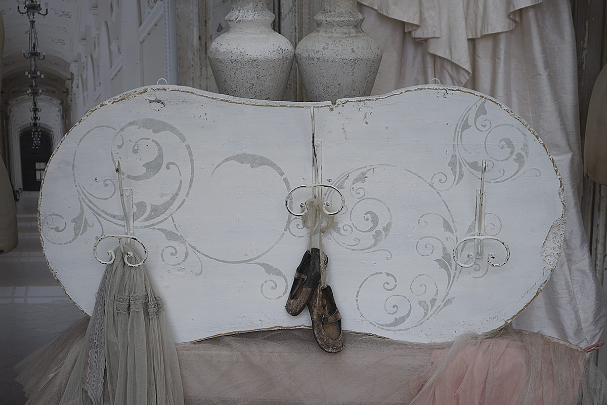 Wand mit eleganten Verzierungen, alten Schuhen und Stoffen in sanften Farbtönen