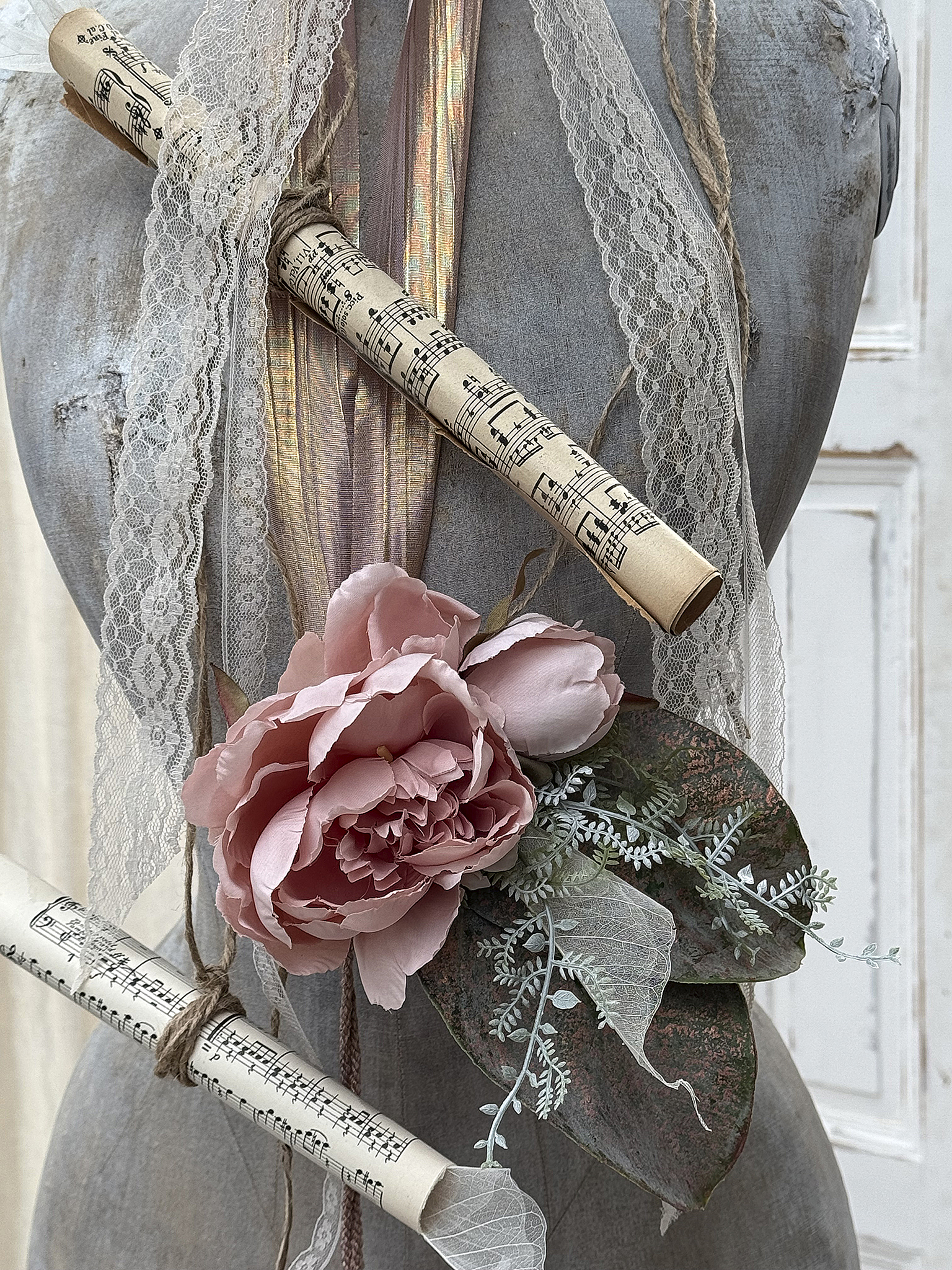 Dekorative Mannequin mit Noten, Spitze und künstlichen Blumen Mannequin verziert mit Notenrollen, Spitze und einer rosafarbenen Blume