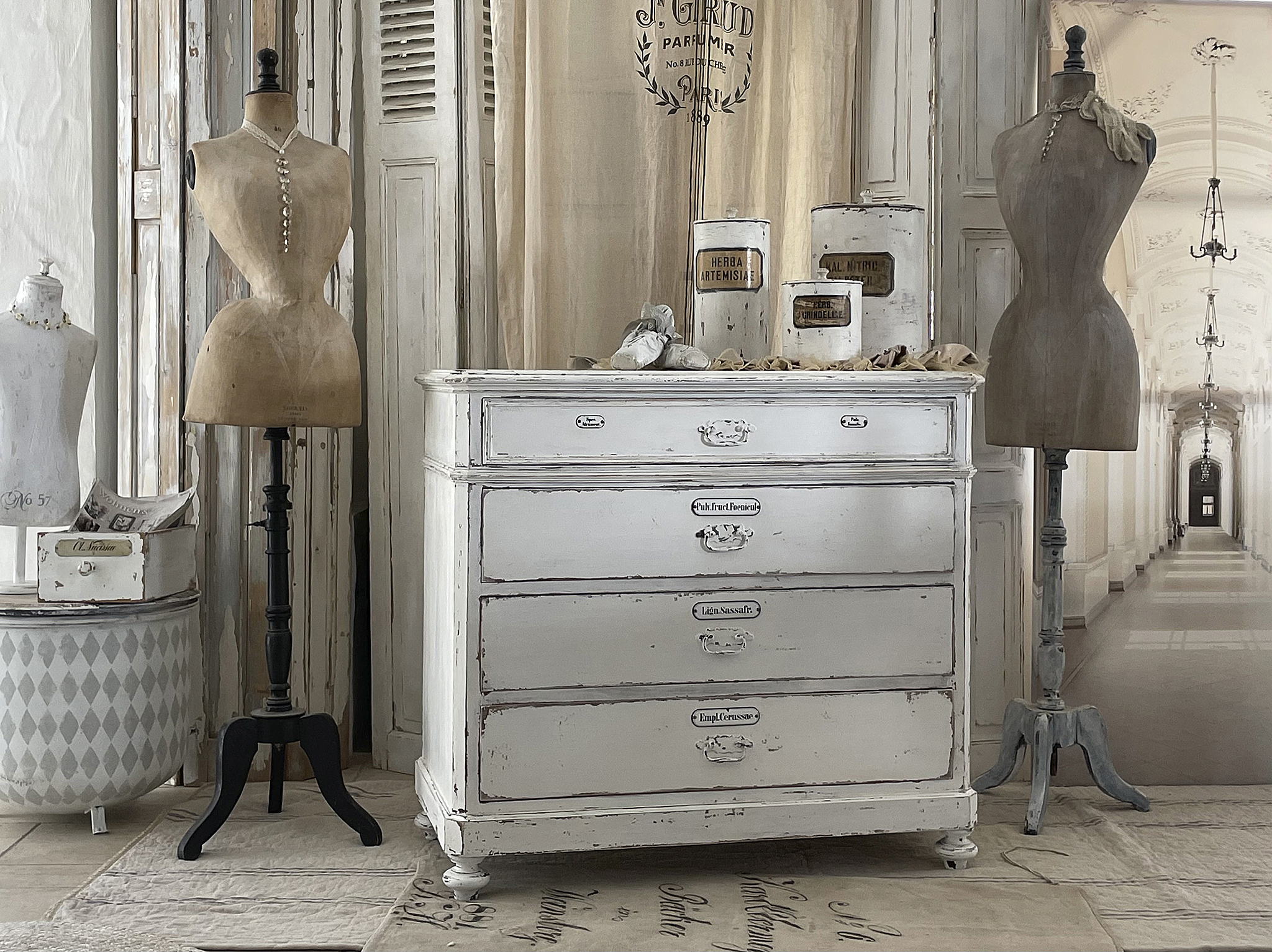 Elegante Kommode in Vintage-Optik mit Schneiderpuppen Weiße Vintage-Kommode mit vier Schubladen und zwei Schneiderpuppen im Hintergrund.