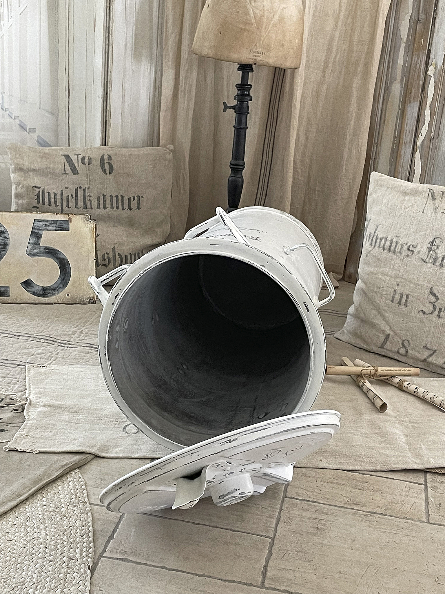 Vintage Eimer mit Dekoration in einem gemütlichen Raum Weißer Vintage Eimer liegt auf dem Boden eines stilvollen Wohnraums mit Kissen und einer Lampe.