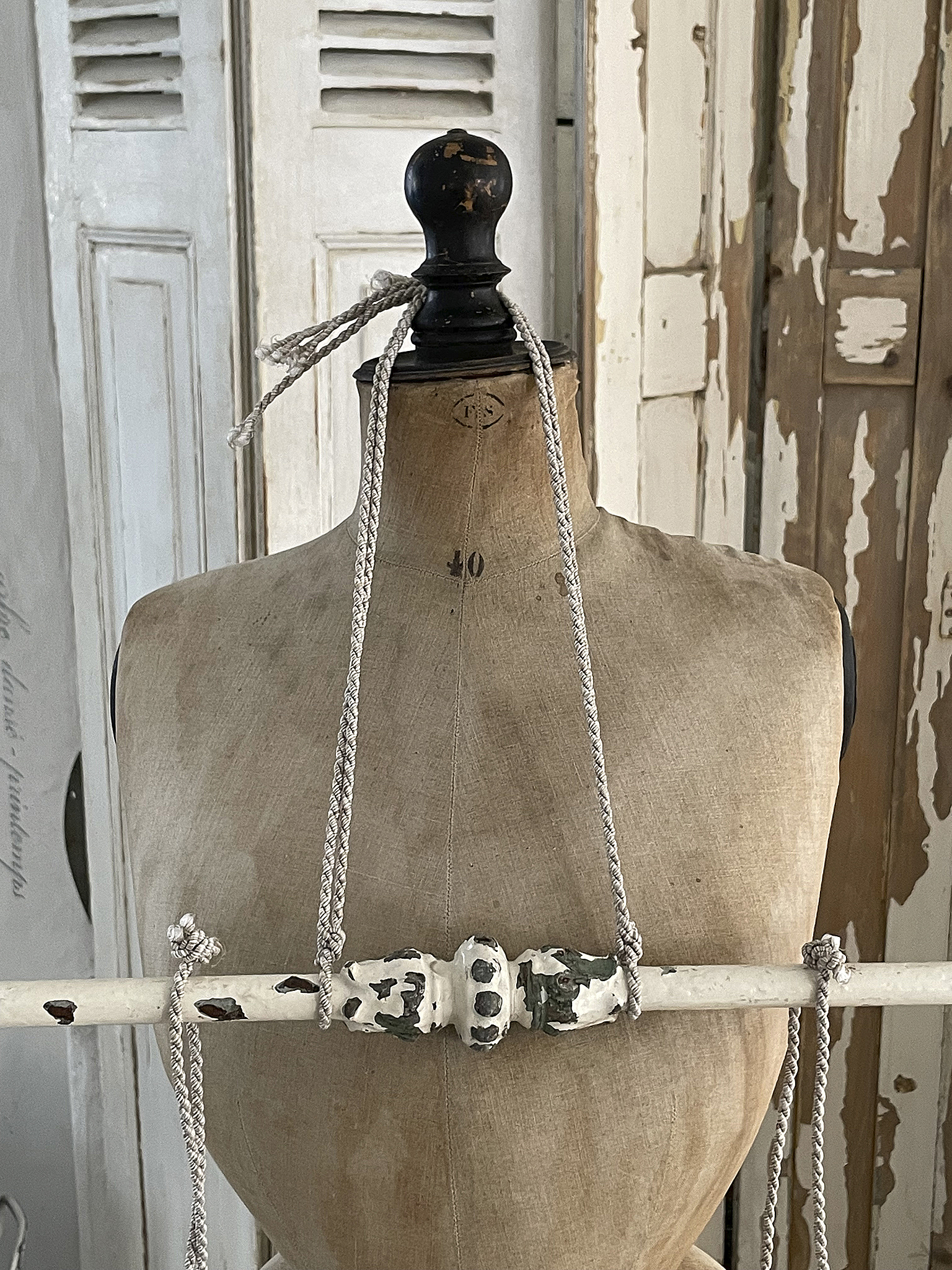 Vintage Schneiderpuppe mit dekorativen Schnüren Schneiderpuppe im Vintage-Stil, verziert mit weißen und grauen Schnüren und einem hellen Hintergrund.
