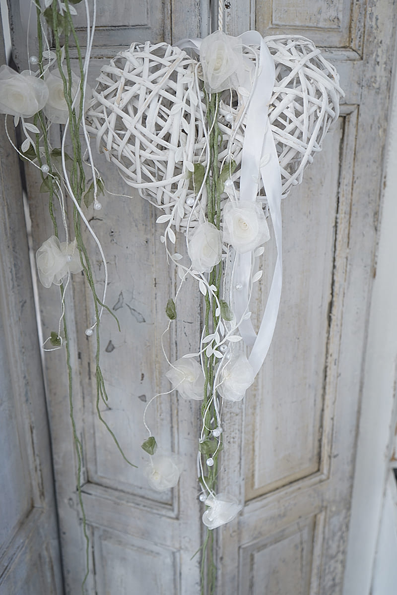 Herzkranz aus Rattan mit weißen Rosen und Schleifen, dekorativ an einer Wand befestigt