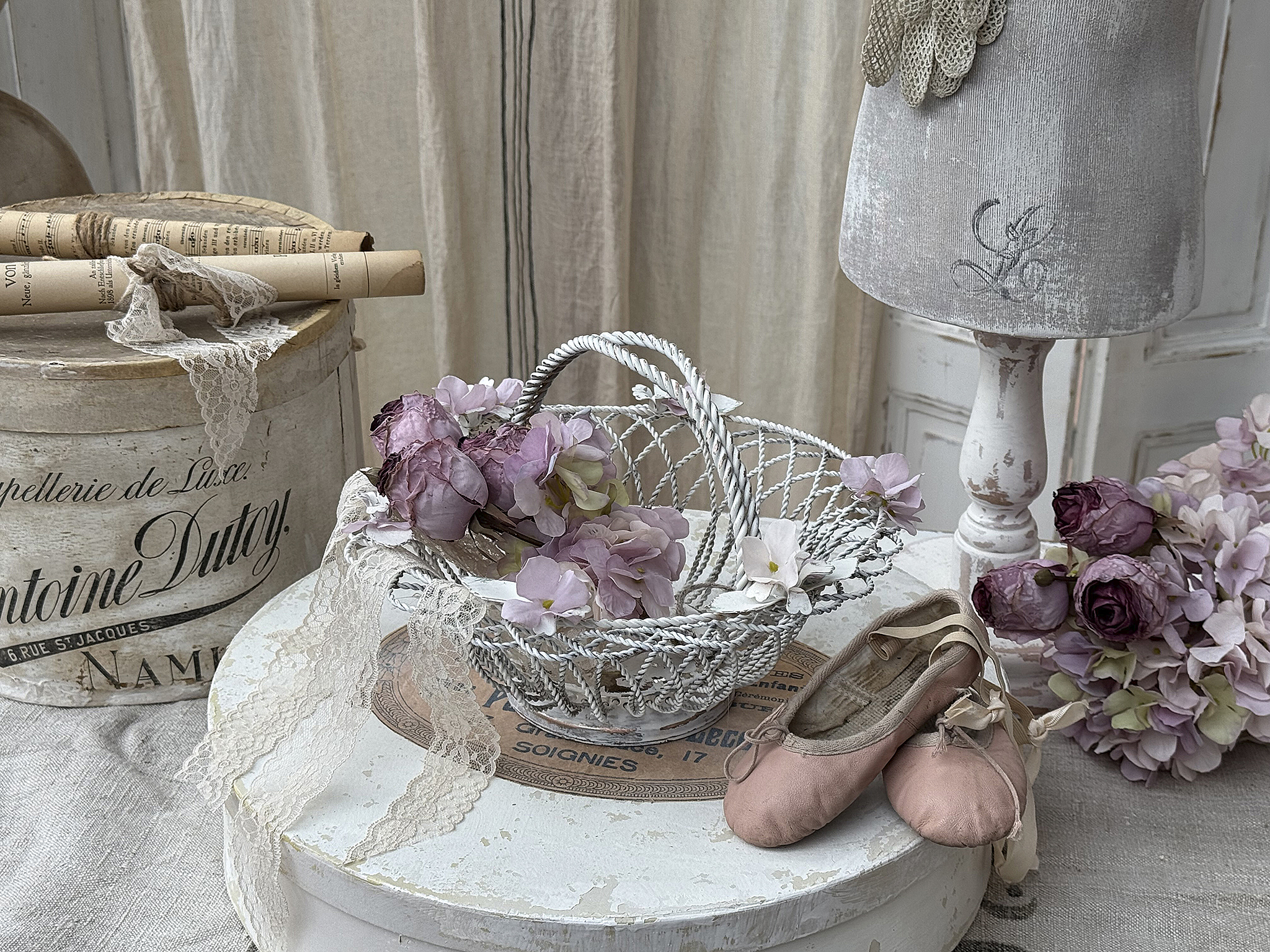 Dekorativer Tisch mit rosa Ballerinas und Blumenarrangement Ein eleganter Tisch mit einem Korb voller Blumen, rosa Ballerinas und Vintage-Dekoration.