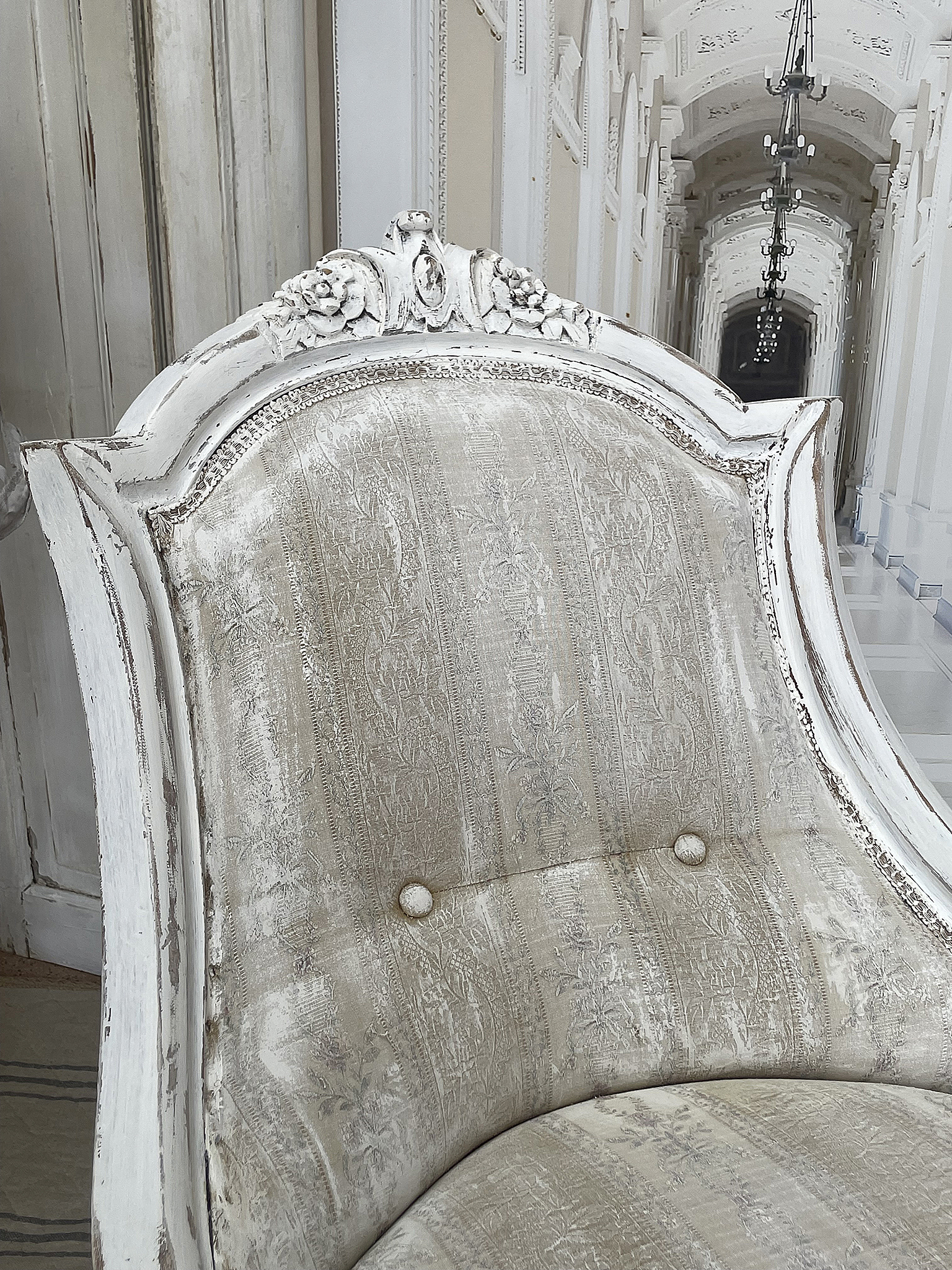 Eleganter antiker Sessel mit zartem Stoffbezug Detailaufnahme eines antiken Sessels mit floralem Stoffbezug und kunstvoll verziertem Holzrahmen.