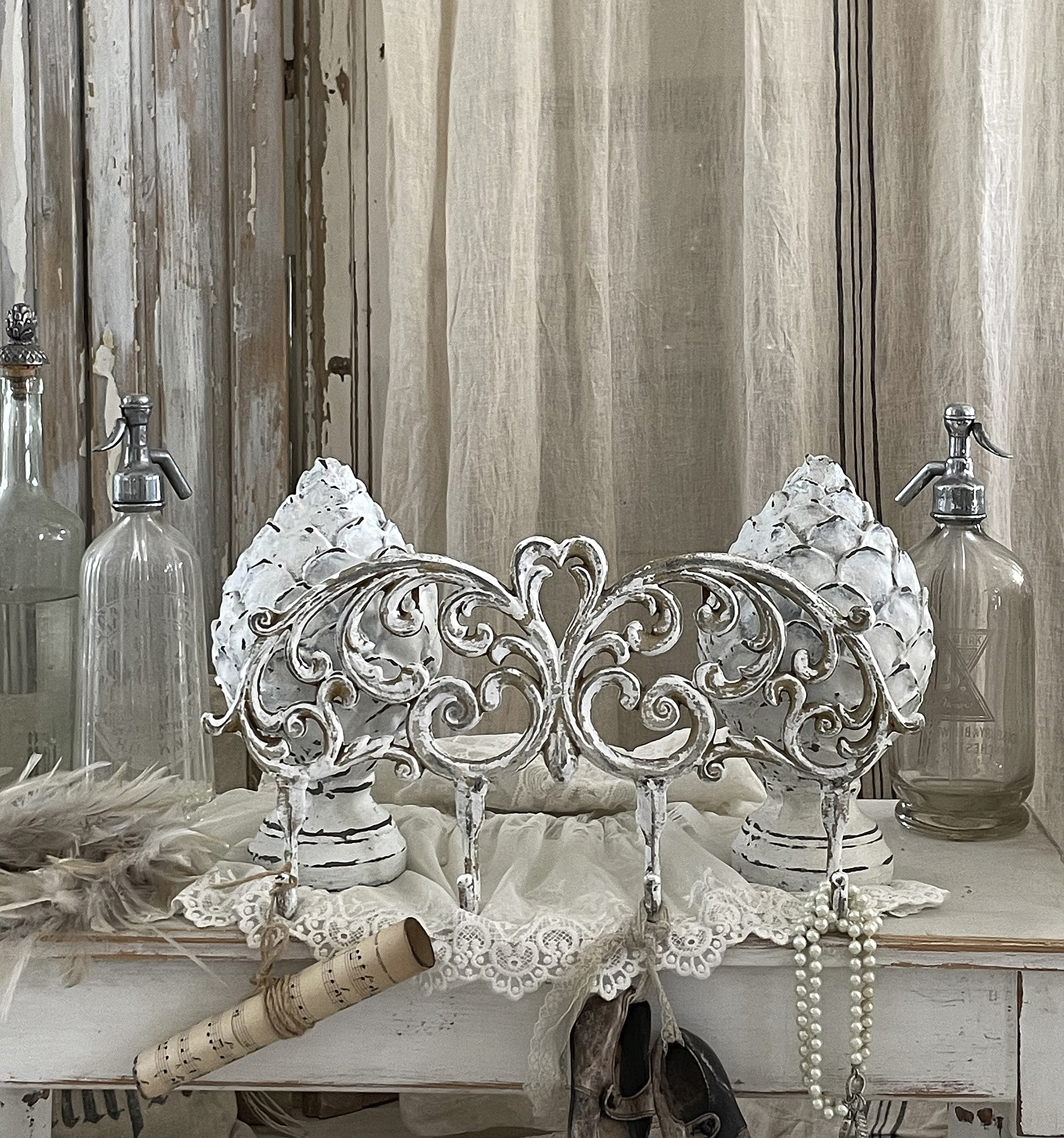 Dekorativer Haken für Schmuck und Accessoires mit floralen Motiven Eleganter Schmuckhalter in Weiß mit floralen Verzierungen, umgeben von vintage Flaschen und Dekorationen.